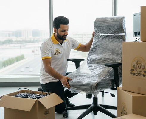 Professional mover wrapping an office chair with protective film during an office move in Dubai.